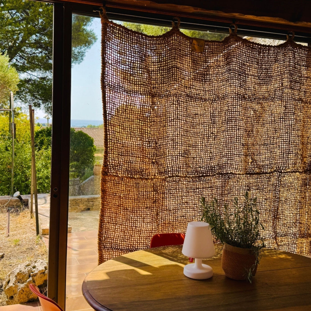 Cortina de fibra de coco junto a una ventana con mesa y lámpara