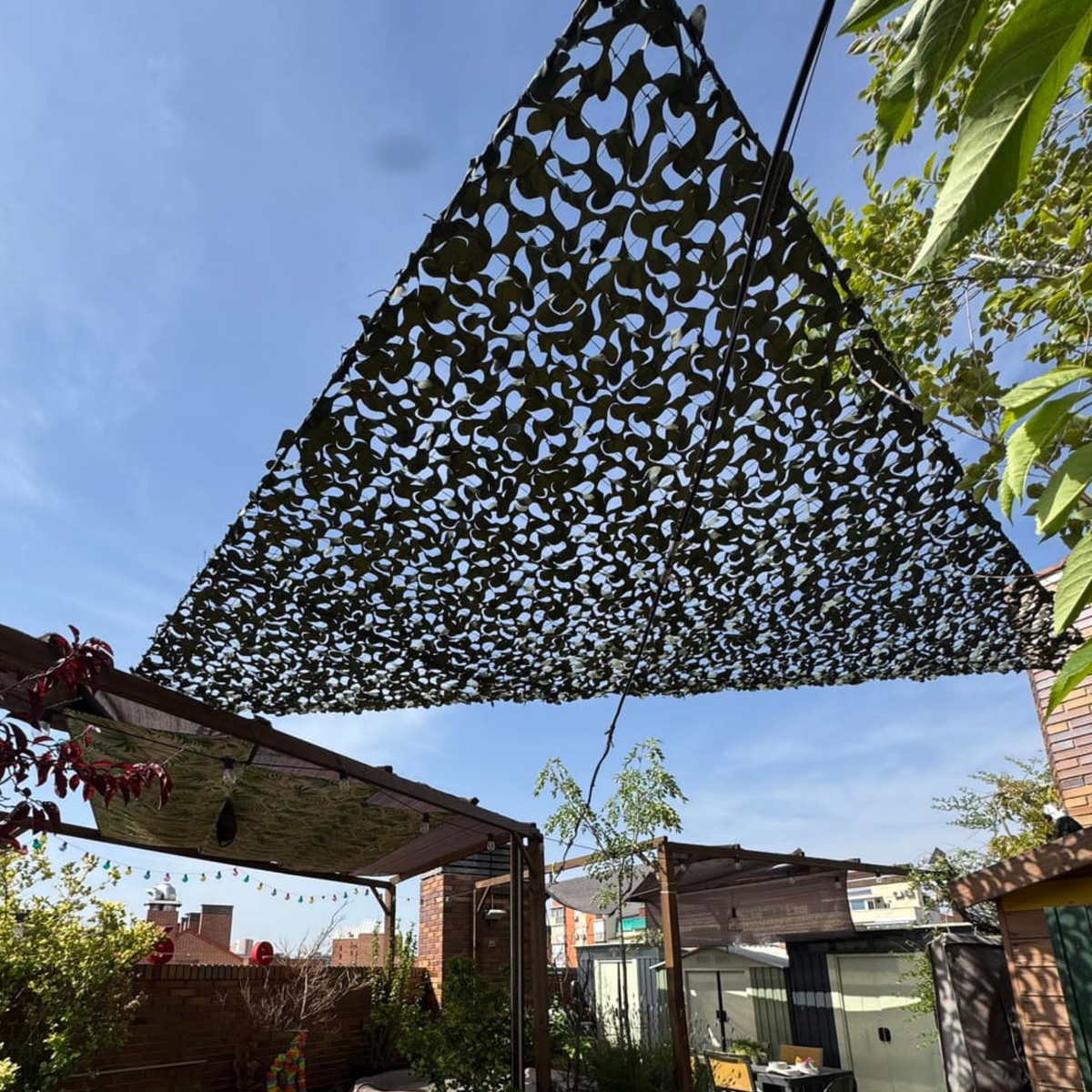 Red de camuflaje triangular oscura sobre una pérgola de jardín